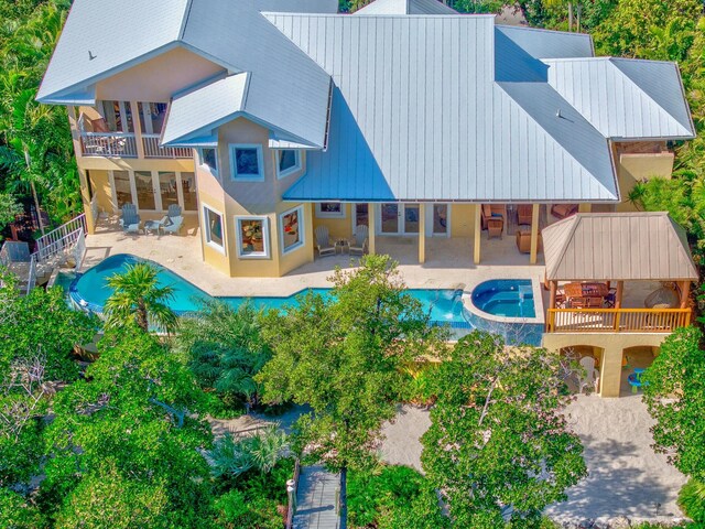 rear view of property featuring metal roof, a pool with connected hot tub, a patio area, and a balcony