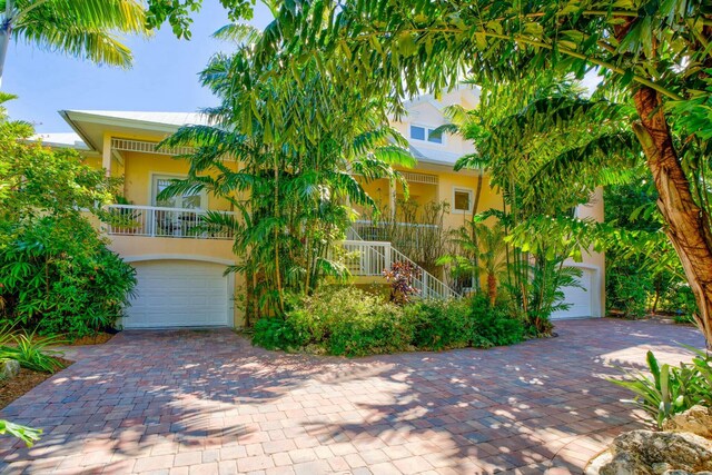 view of property hidden behind natural elements with decorative driveway, stucco siding, covered porch, stairway, and a garage