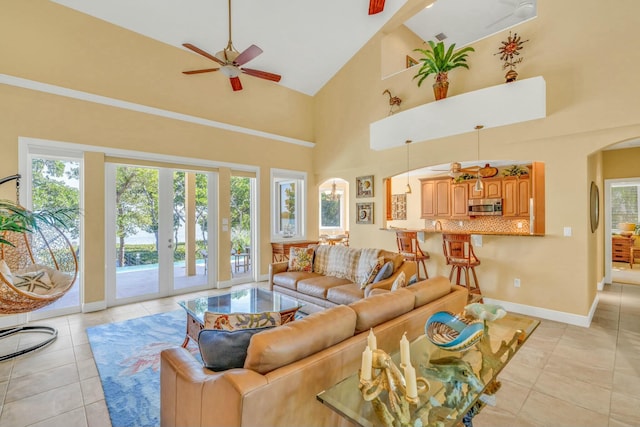 living room featuring arched walkways, high vaulted ceiling, light tile patterned flooring, and baseboards