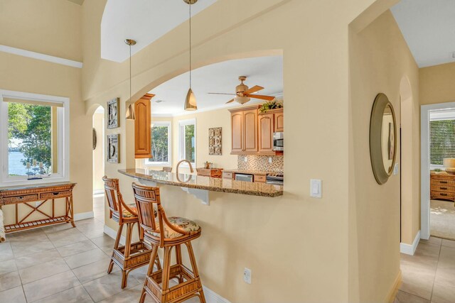 kitchen featuring light tile patterned floors, light stone countertops, stainless steel appliances, a kitchen bar, and backsplash