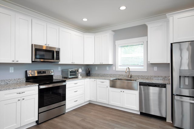 kitchen with sink, hardwood / wood-style flooring, appliances with stainless steel finishes, white cabinetry, and light stone counters