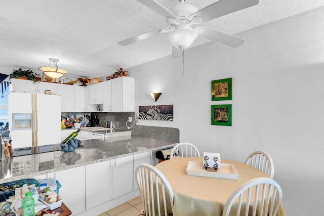 kitchen featuring white cabinetry, white fridge with ice dispenser, light tile patterned floors, light stone counters, and kitchen peninsula