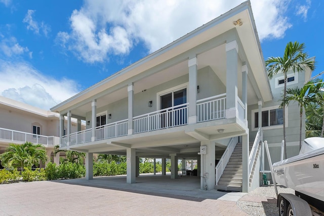 rear view of property with stucco siding, driveway, a carport, and stairs