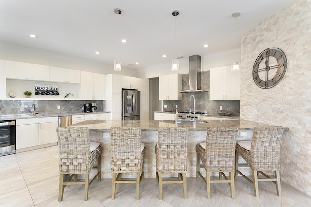 kitchen featuring a kitchen breakfast bar, light stone counters, wall chimney exhaust hood, and stainless steel fridge