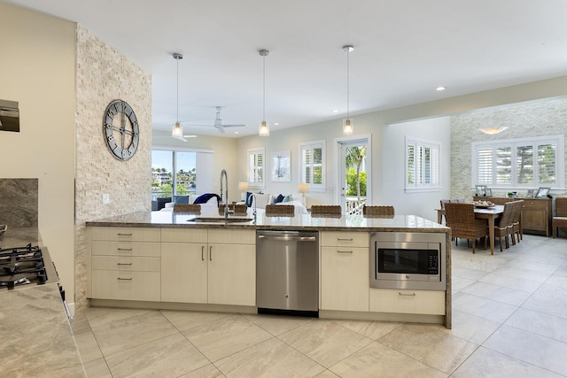 kitchen with open floor plan, appliances with stainless steel finishes, light stone countertops, and a sink