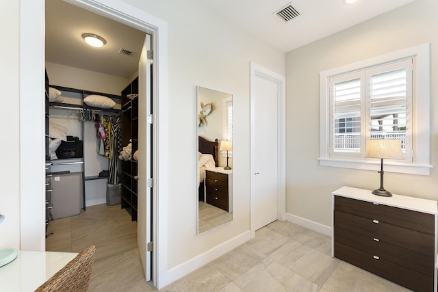 full bath featuring vanity, a walk in closet, baseboards, and visible vents