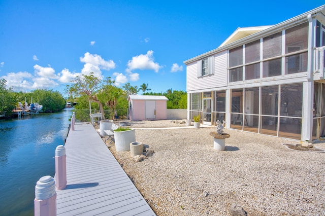 exterior space featuring a storage unit, a water view, a sunroom, a boat dock, and an outdoor structure