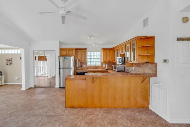 kitchen featuring a peninsula, visible vents, vaulted ceiling, appliances with stainless steel finishes, and glass insert cabinets