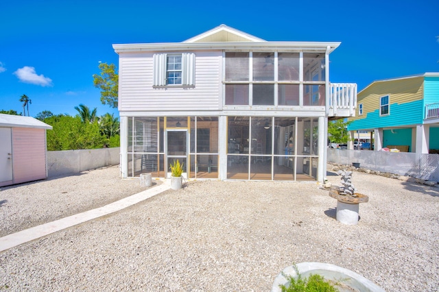 rear view of property featuring an outbuilding, a sunroom, fence, and a storage unit