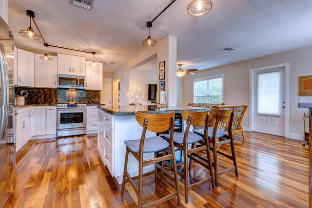 kitchen featuring stainless steel appliances, decorative light fixtures, and white cabinets