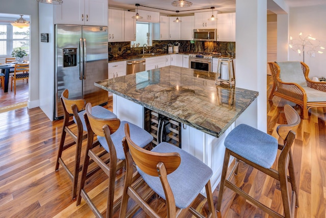 kitchen featuring decorative light fixtures, sink, white cabinets, dark stone counters, and stainless steel appliances