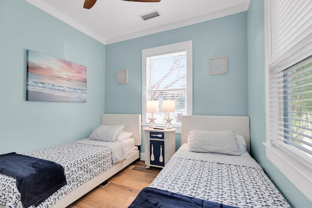 bedroom with ceiling fan, multiple windows, wood finished floors, and visible vents