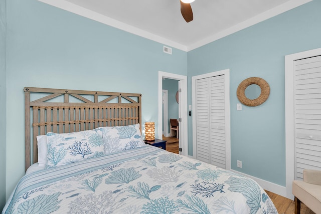 bedroom featuring multiple closets, a ceiling fan, baseboards, wood finished floors, and visible vents