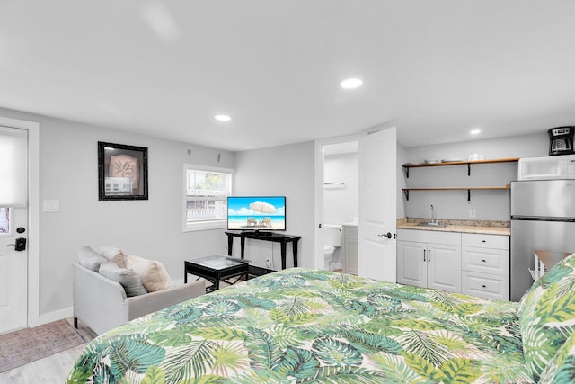 bedroom featuring a sink, light wood finished floors, freestanding refrigerator, recessed lighting, and indoor wet bar