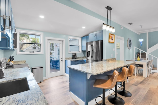 kitchen with blue cabinetry, a kitchen bar, stainless steel refrigerator with ice dispenser, a peninsula, and light wood-style flooring