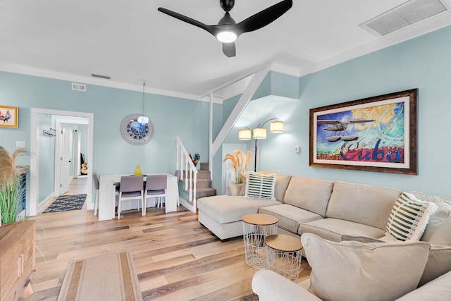 living area featuring stairs, a ceiling fan, visible vents, and light wood finished floors