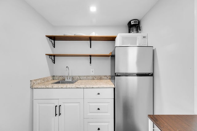 kitchen with open shelves, a sink, white cabinets, freestanding refrigerator, and white microwave