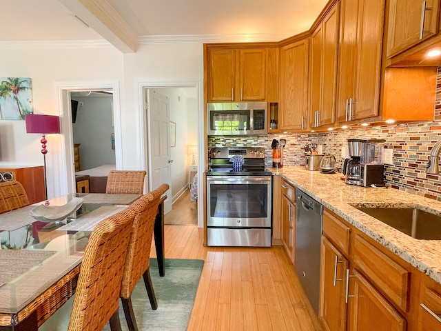 kitchen with light stone counters, ornamental molding, stainless steel appliances, light hardwood / wood-style floors, and decorative backsplash