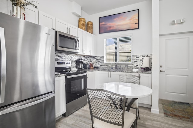 kitchen with stainless steel appliances, white cabinetry, backsplash, and light stone counters