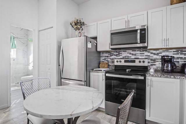 kitchen with light stone counters, stainless steel appliances, backsplash, and white cabinets