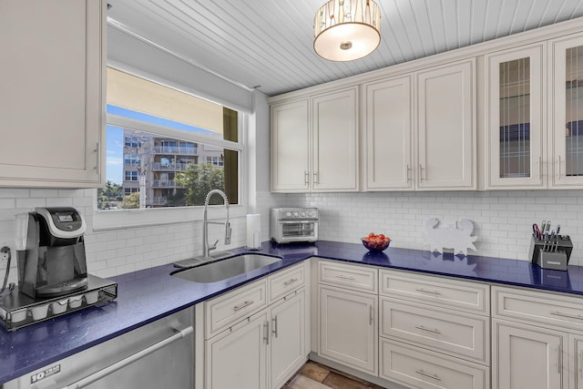 kitchen featuring tasteful backsplash, dishwasher, sink, and white cabinetry