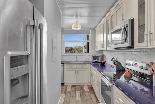 kitchen with sink, tasteful backsplash, hanging light fixtures, light wood-type flooring, and appliances with stainless steel finishes