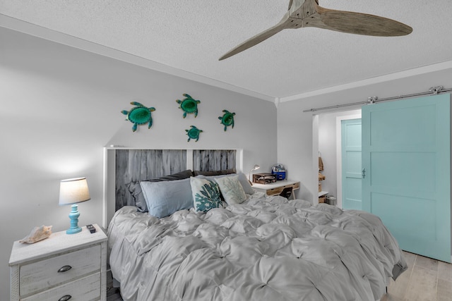 bedroom with ceiling fan, ornamental molding, a textured ceiling, a barn door, and light wood-type flooring