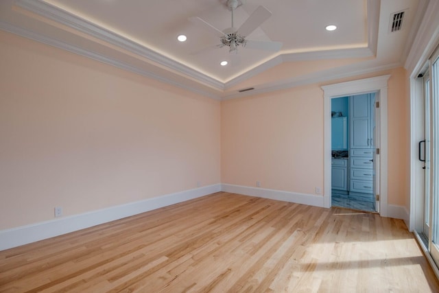 empty room with crown molding, a tray ceiling, light hardwood / wood-style floors, and ceiling fan