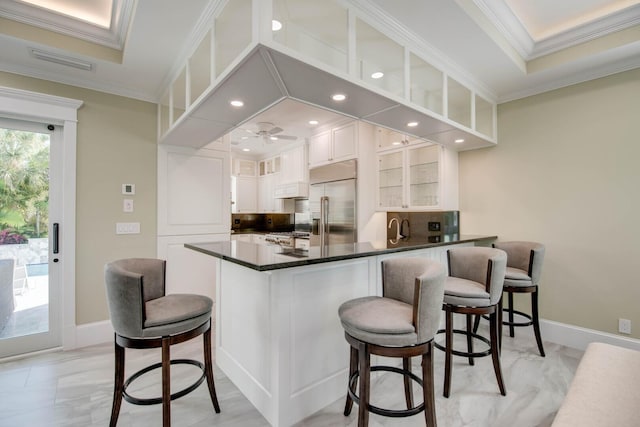 kitchen featuring stainless steel built in refrigerator, kitchen peninsula, a breakfast bar area, and white cabinets