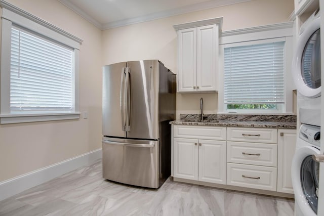 kitchen featuring stacked washer and dryer, dark stone countertops, white cabinets, and stainless steel fridge