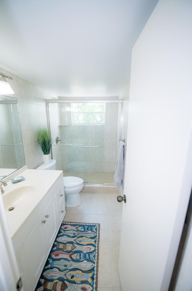 bathroom featuring toilet, tile walls, vanity, a shower with door, and tile patterned flooring