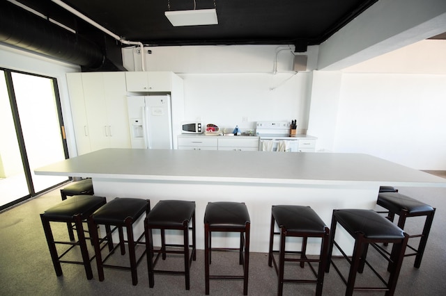 kitchen with white cabinetry, a breakfast bar, and white appliances