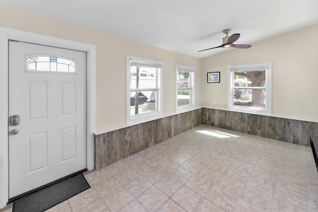 foyer featuring ceiling fan and wood walls