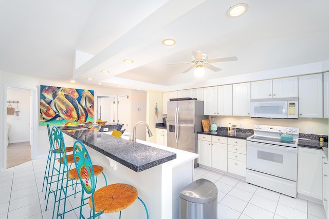 kitchen with a ceiling fan, light tile patterned flooring, a kitchen breakfast bar, and white appliances