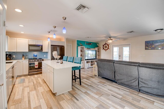 kitchen with a kitchen island, appliances with stainless steel finishes, white cabinets, decorative backsplash, and hanging light fixtures