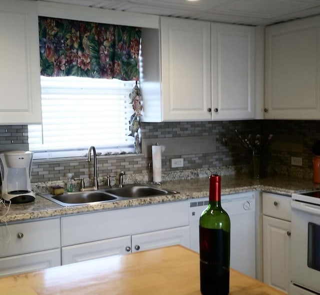 kitchen with sink, stove, tasteful backsplash, light stone countertops, and white cabinets