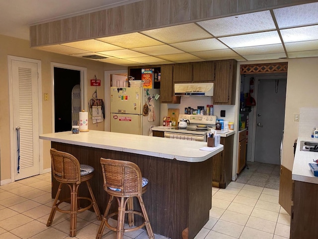 kitchen with stainless steel electric range, dark brown cabinets, light tile patterned flooring, kitchen peninsula, and white fridge