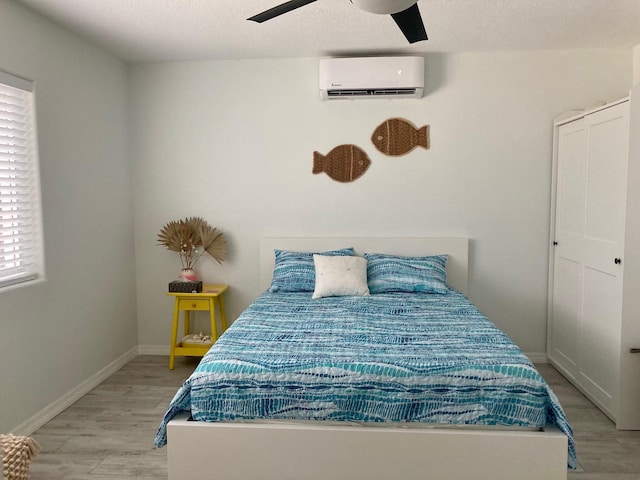 bedroom featuring a wall mounted AC, a textured ceiling, ceiling fan, and light hardwood / wood-style flooring