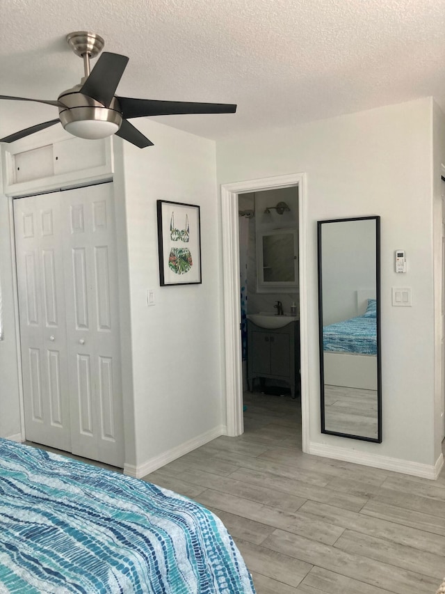 bedroom with ensuite bath, light hardwood / wood-style flooring, ceiling fan, a textured ceiling, and a closet