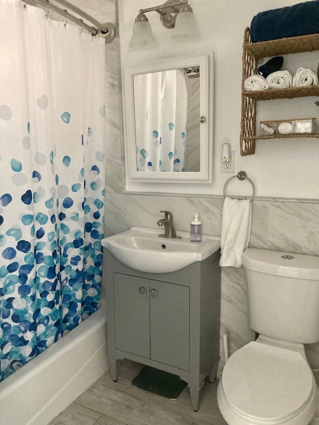 full bathroom featuring tile walls, hardwood / wood-style flooring, vanity, toilet, and shower / bath combo