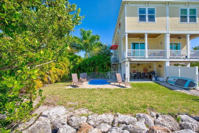 rear view of house with a patio area, a balcony, a lawn, ceiling fan, and a fenced in pool