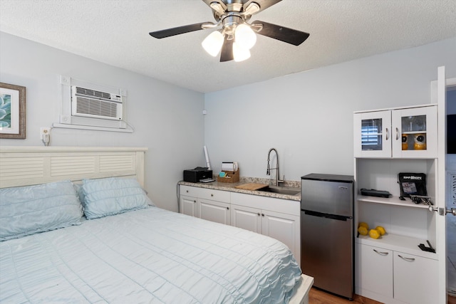 bedroom featuring a wall mounted air conditioner, a sink, a textured ceiling, freestanding refrigerator, and ceiling fan