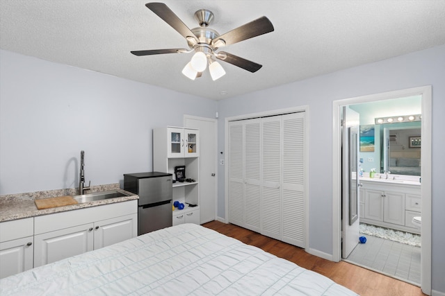 bedroom with freestanding refrigerator, wood finished floors, a closet, a textured ceiling, and a sink