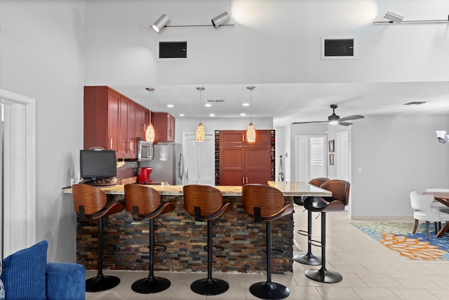 kitchen featuring a peninsula, stainless steel appliances, pendant lighting, a kitchen bar, and reddish brown cabinets