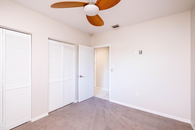 unfurnished bedroom featuring a ceiling fan, baseboards, visible vents, light carpet, and two closets