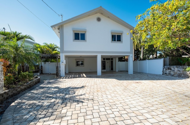 view of front of property featuring stucco siding, decorative driveway, a carport, and fence