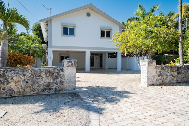 raised beach house featuring stucco siding, decorative driveway, a carport, and fence