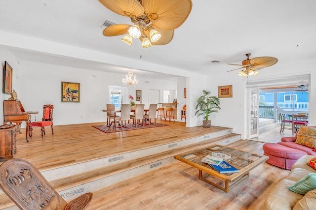 living area with wood finished floors, visible vents, and ceiling fan with notable chandelier