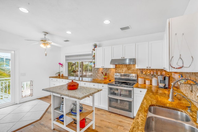 kitchen with open shelves, under cabinet range hood, range with two ovens, and a sink