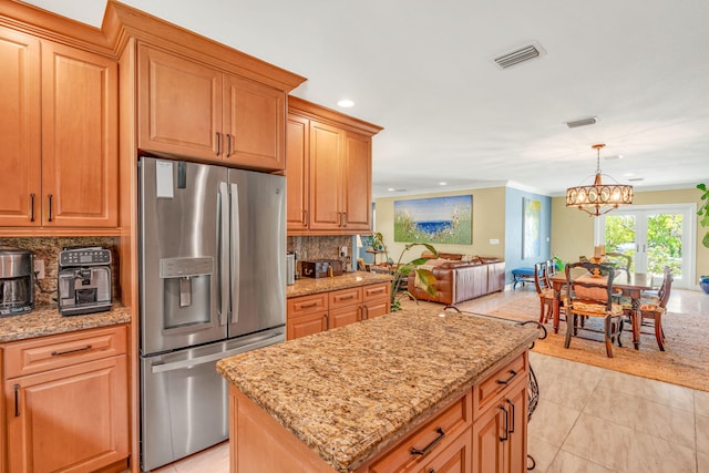 kitchen with a center island, stainless steel refrigerator with ice dispenser, tasteful backsplash, light stone counters, and decorative light fixtures